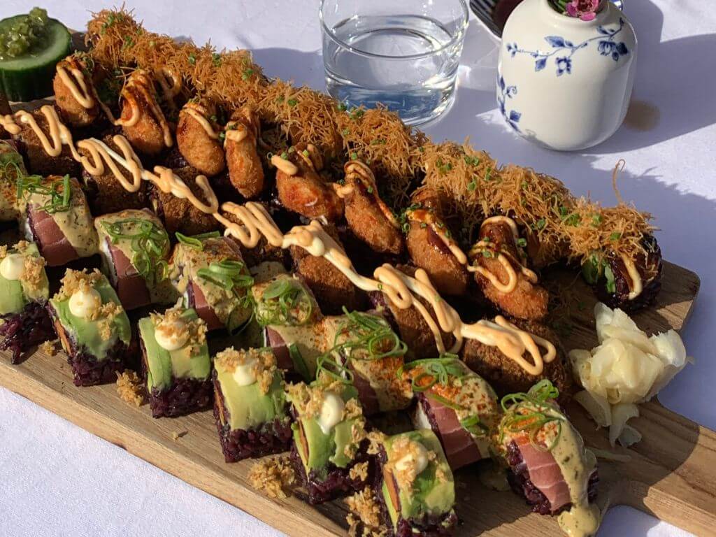 A large, colorful sushi platter served during a luxury Amsterdam brunch boat tour, featuring tuna rolls with avocado and crispy fried toppings on a wooden board