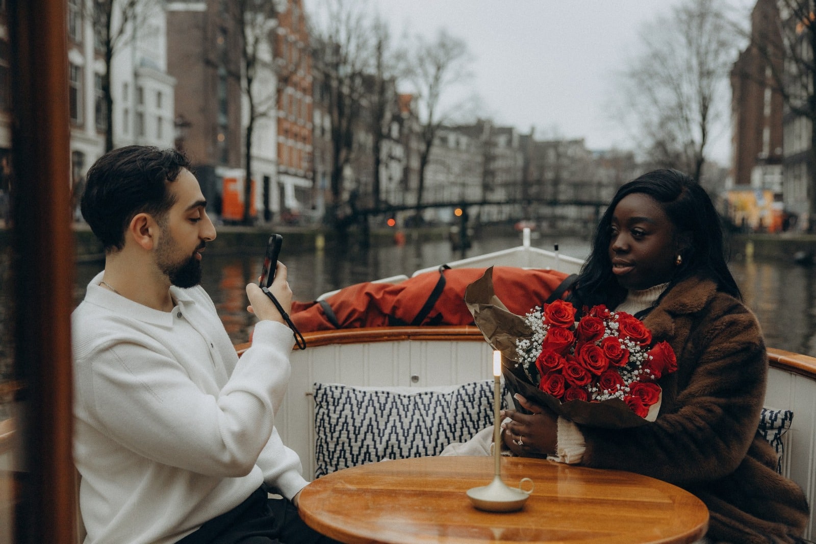 Un chico fotografiando a su prometida con rosas rojas en un crucero de invierno por los canales de &Aacute;msterdam